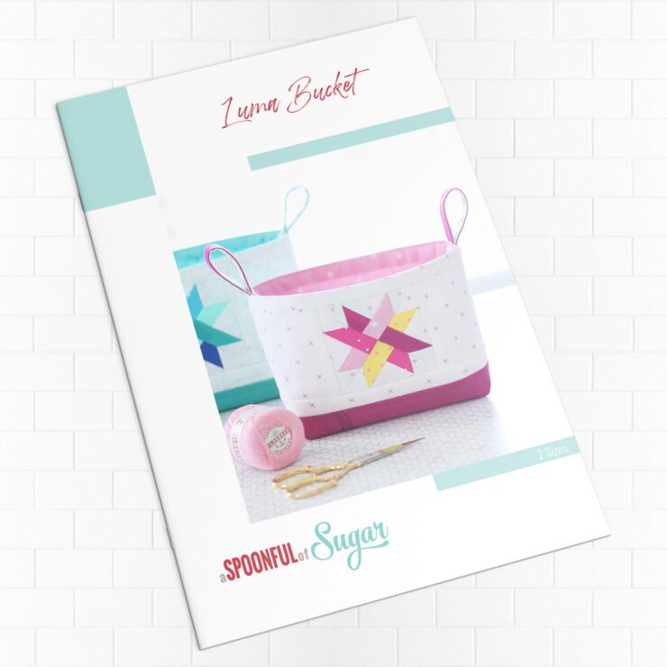 Two Luma Bucket fabric organisers in bright Ruby Star Society prints, one pink and one green, shown side‑by‑side to display the woven star panel and contrast base. Pattern by A Spoonful of Sugar Designs. 