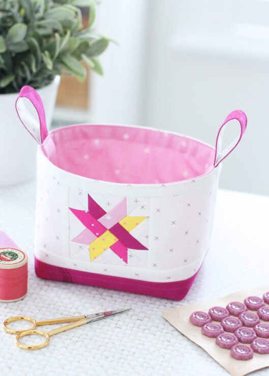 Two Luma Bucket fabric organisers in bright Ruby Star Society prints, one pink and one green, shown side‑by‑side to display the woven star panel and contrast base. Pattern by A Spoonful of Sugar Designs. 