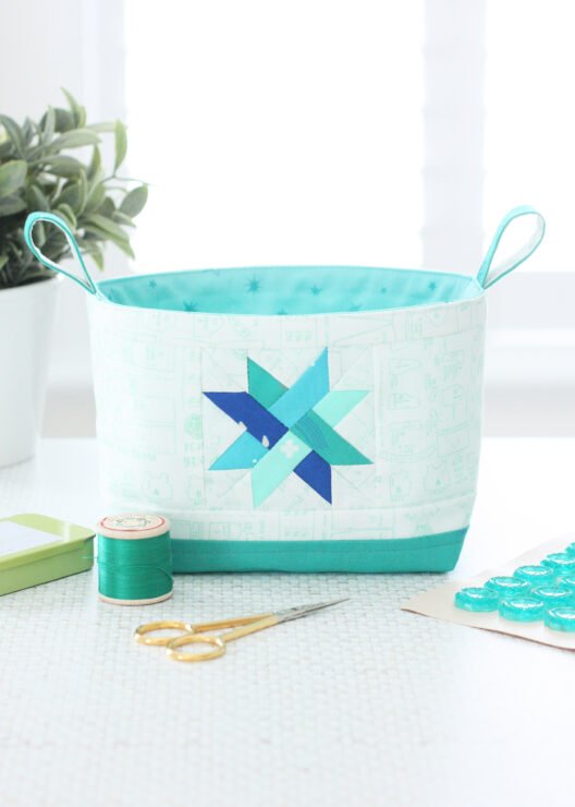 Two Luma Bucket fabric organisers in bright Ruby Star Society prints, one pink and one green, shown side‑by‑side to display the woven star panel and contrast base. Pattern by A Spoonful of Sugar Designs. 