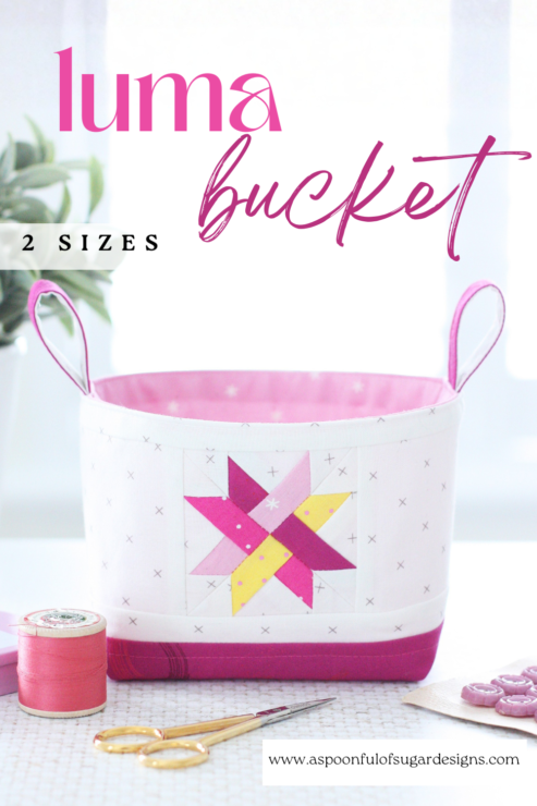 Two Luma Bucket fabric organisers in bright Ruby Star Society prints, one pink and one green, shown side‑by‑side to display the woven star panel and contrast base. Pattern by A Spoonful of Sugar Designs. 