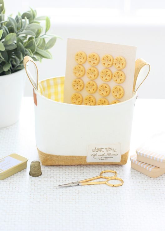 Luma Bucket sewing pattern filled with sewing notions including buttons, scissors, pins, and a thimble for organized craft storage.